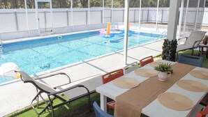 Area piscina esterna coperta con tavolo e sedie, una piccola struttura giochi e un cortile recintato.