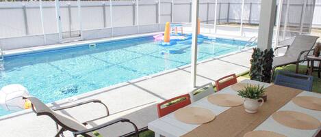 A covered outdoor pool area with a table and chairs, a small play structure, and a fenced yard.