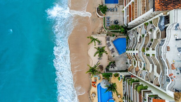 Vista aérea de un hotel frente al mar con piscina, sillas de playa y una pequeña zona de arena.