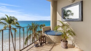 Un balcón con vista a la playa y al océano, una silla, un taburete pequeño y dos plantas en macetas.