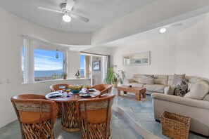Ein geräumiges Wohnzimmer mit einem großen Sofa, einem Esstisch mit Stühlen und einem Deckenventilator.
