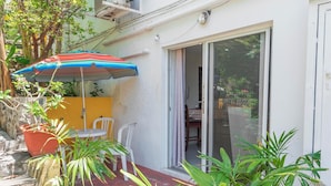 Un patio con mesa y sillas, un parasol colorido y plantas en macetas.