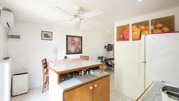 Una cocina compacta con una mesa de comedor, sillas, ventilador de techo, refrigerador y obras de arte colgadas en la pared.