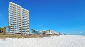 Un hotel frente a la playa con varios balcones, una playa de arena y un cielo azul despejado.
