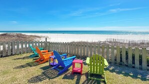 Vista de una playa con una cerca de madera y sillas Adirondack de colores.