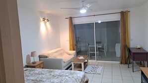 Habitació d'hotel amb un llit, una taula de treball, una cadira, una taula petita, una làmpada, un ventilador de sostre i una porta corredissa de vidre que dona a un balcó.