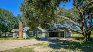 Une maison à deux étages avec une cheminée en briques, un garage fermé et un grand arbre dans le jardin.