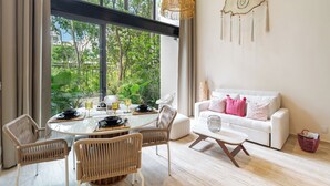 Een moderne woonkamer met een eethoek, grote ramen en een witte bank met roze kussens.