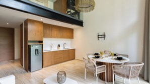 Een moderne keuken met een inbouwkoelkast, houten kasten en een eethoek met een ronde tafel en rieten stoelen.
