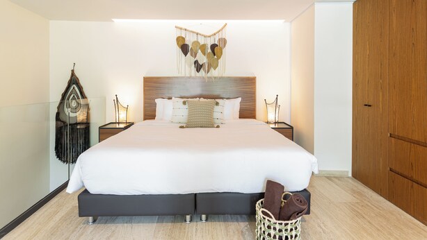 Een moderne slaapkamer met een groot bed, een houten hoofdbord, nachtkastjes en een decoratieve wandhanger.