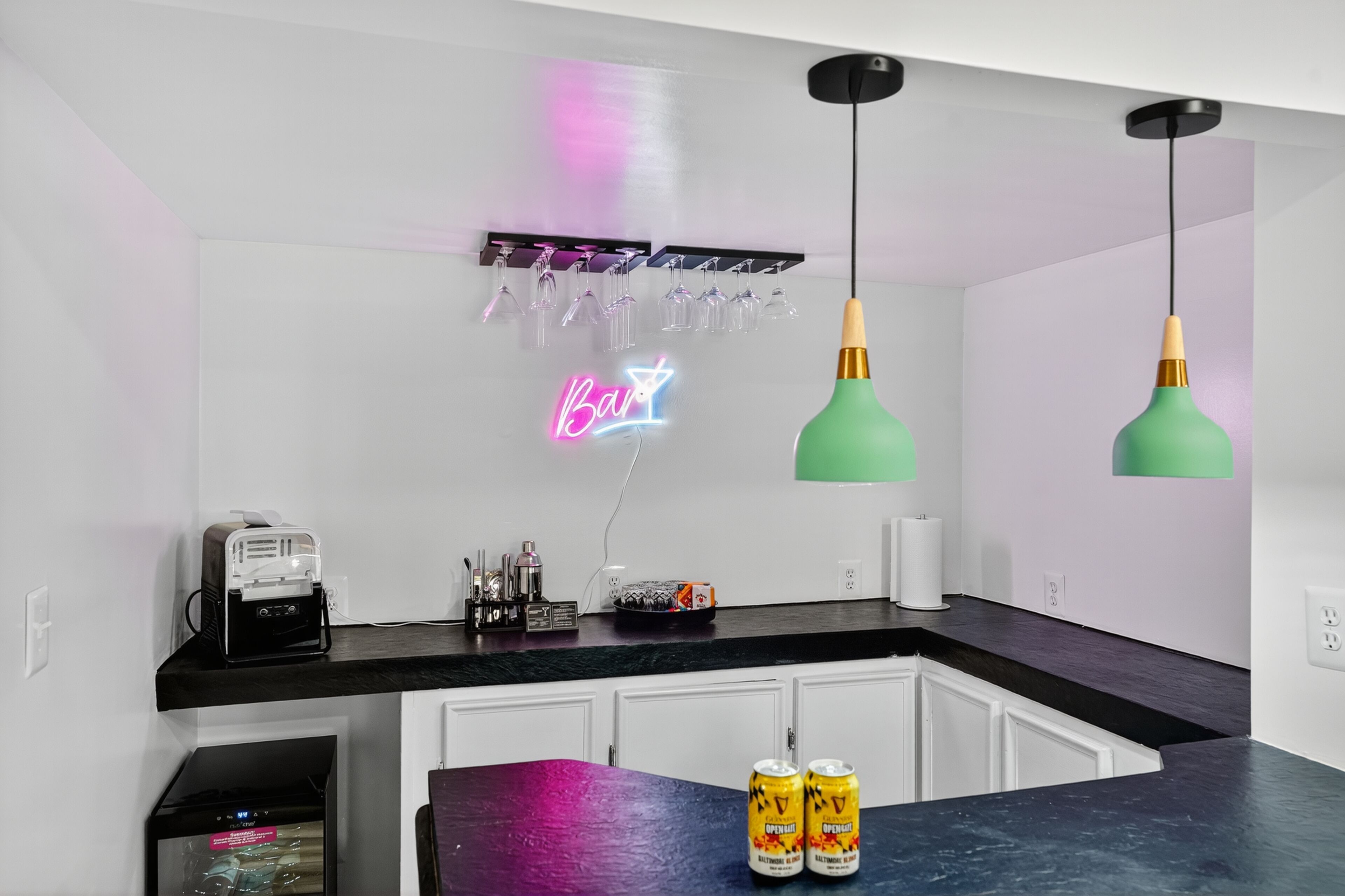 A modern kitchen with a neon sign reading "Bar", a projector, and two green pendant lights.