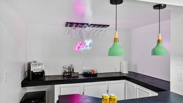 A modern kitchen with a neon sign reading "Bar", a projector, and two green pendant lights.
