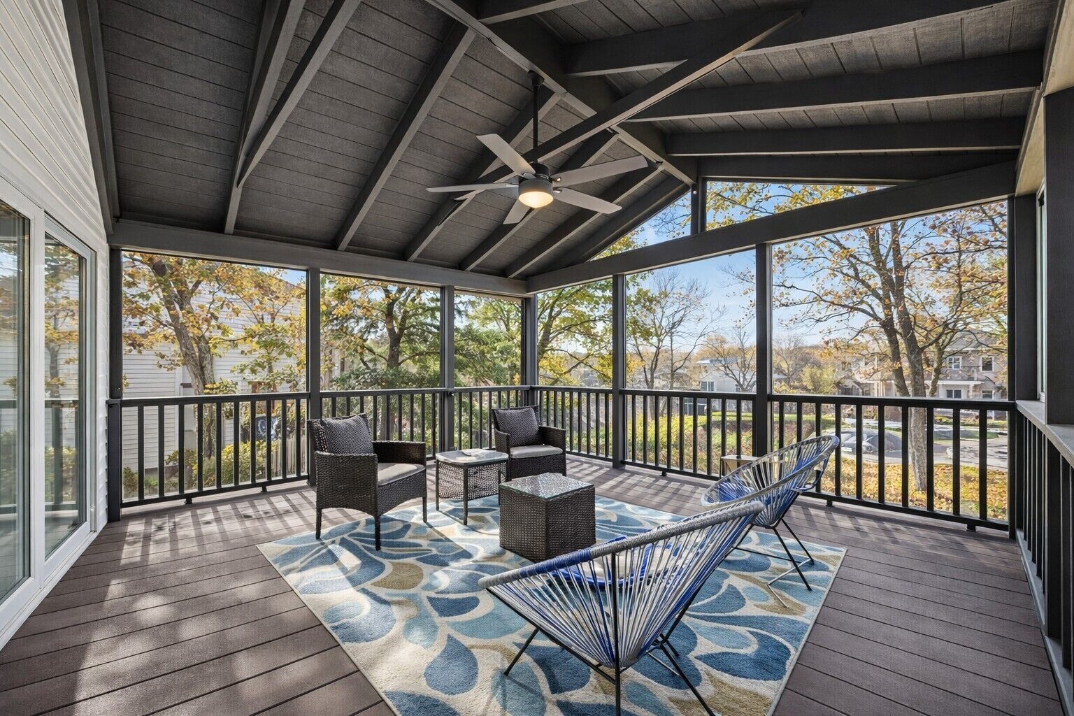 Une terrasse extérieure couverte, dotée d’un ventilateur de plafond, de meubles en osier et d’un tapis à motifs.
