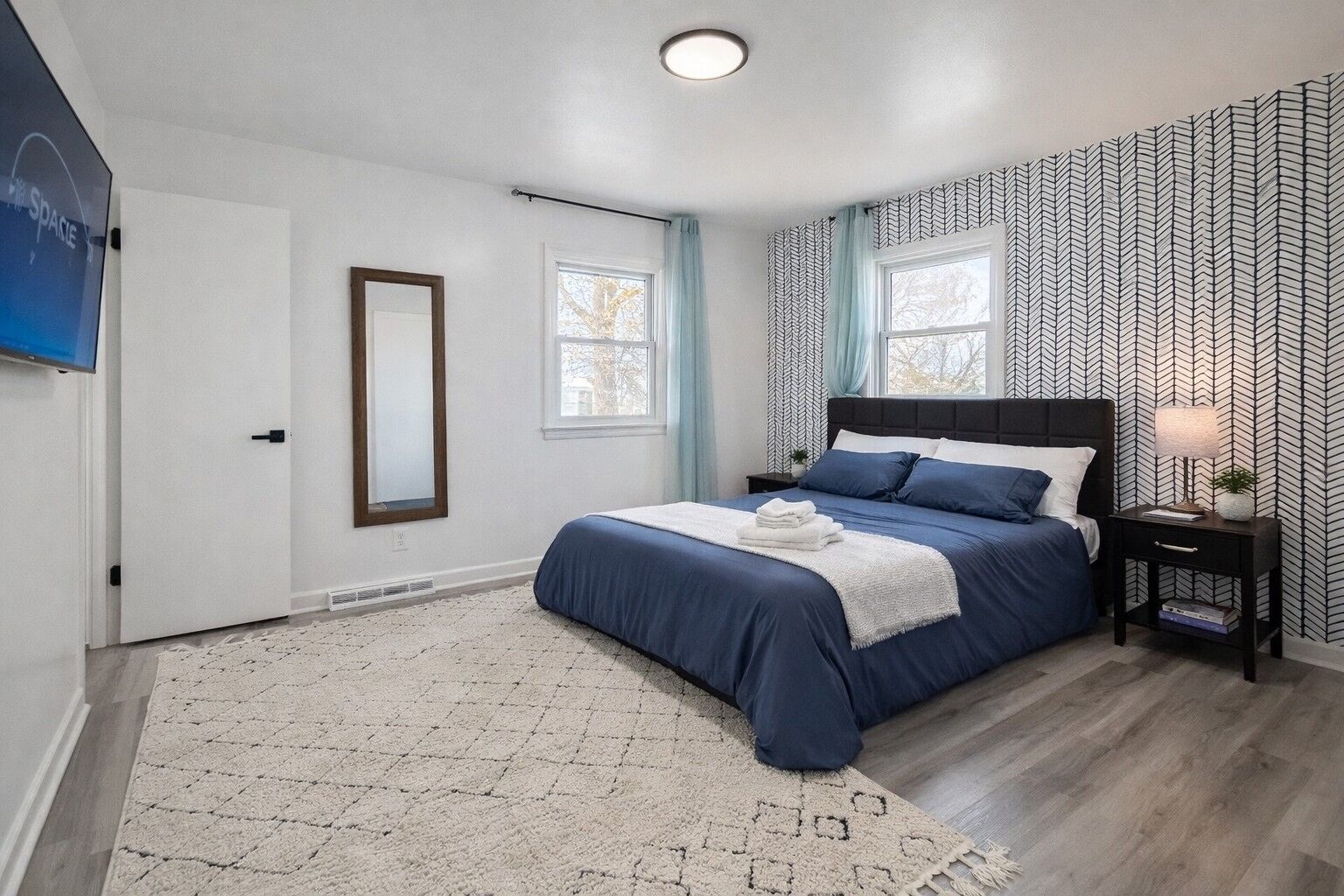 Une chambre à coucher avec un lit, une table de chevet, un miroir et un papier peint à motifs.