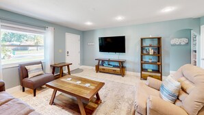 A living room with a wooden coffee table, two sofas, a TV, and a bookshelf. - Bright Beachy 3BR Melbourne House—Dog‑Friendly with Screened Patio + Prime Location☀️🐕 (Melbourne)