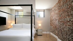 Ein modernes Schlafzimmer mit einem Himmelbett, einem kleinen Nachttisch mit Lampe, einem Beistelltisch und einer Ziegelwand.