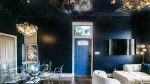 Ein modernes Wohnzimmer mit einer dunkelblauen Tür, durchsichtigen Glastischen, einem weißen Sofa und einer Kristallleuchtre.