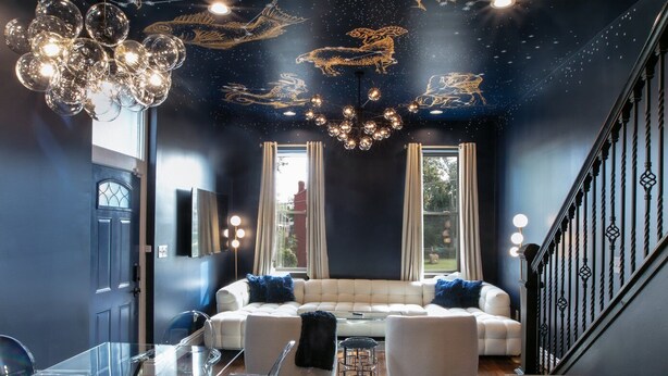 Ein modernes Wohnzimmer mit einer dunkelblauen Wand, einem weißen Sofa und einem klaren Glastisch mit Stühlen.