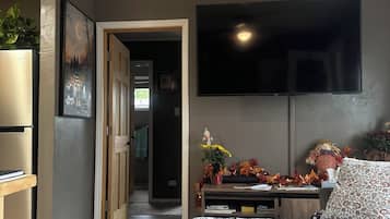Une chambre à coucher comprenant un lit, un téléviseur à écran plat, un bureau avec une plante et une porte donnant sur une autre pièce.