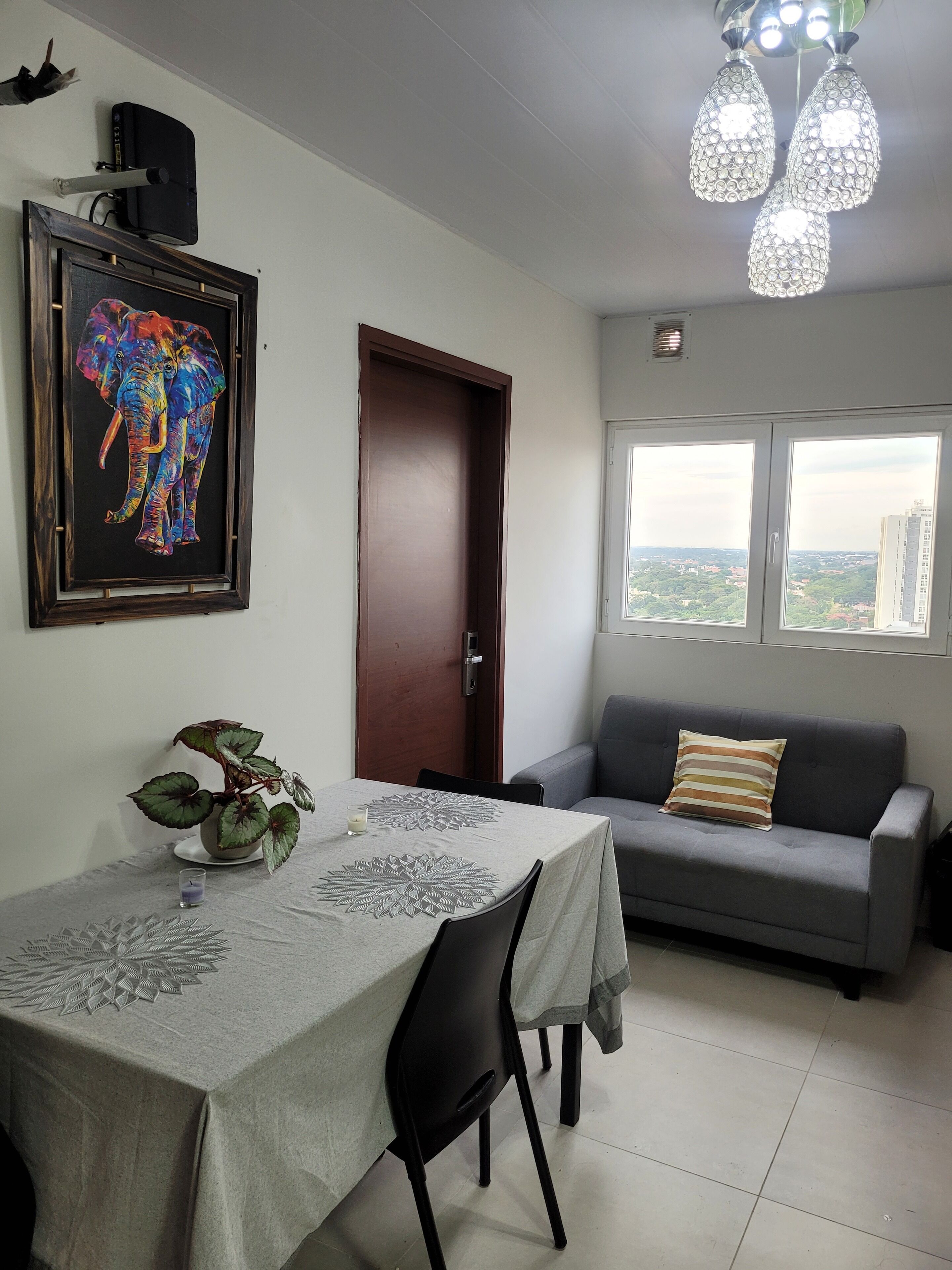 Un comedor con una mesa, sillas, una planta y un cuadro en la pared.