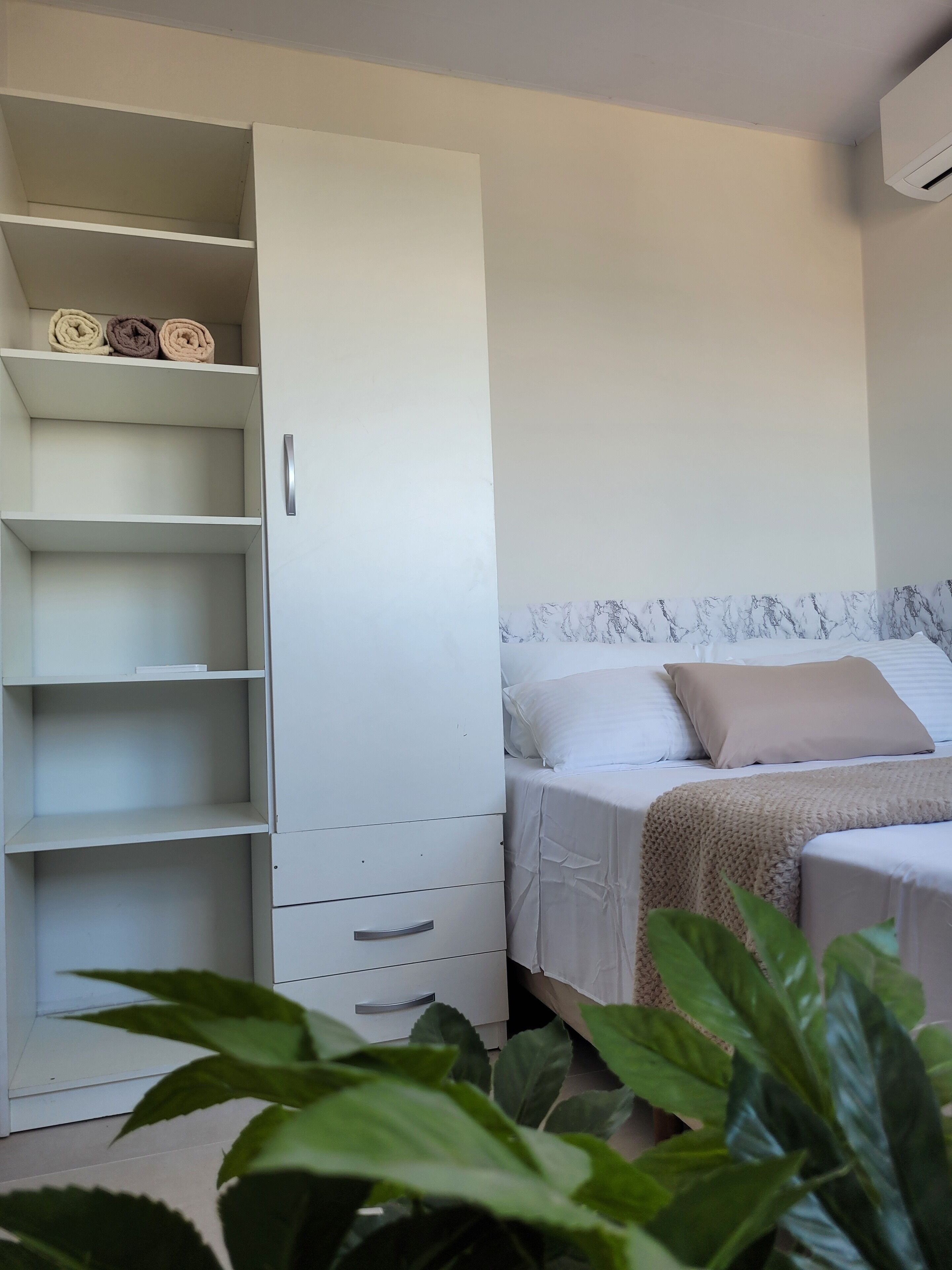 Un dormitorio con cama, armario blanco y planta en maceta.