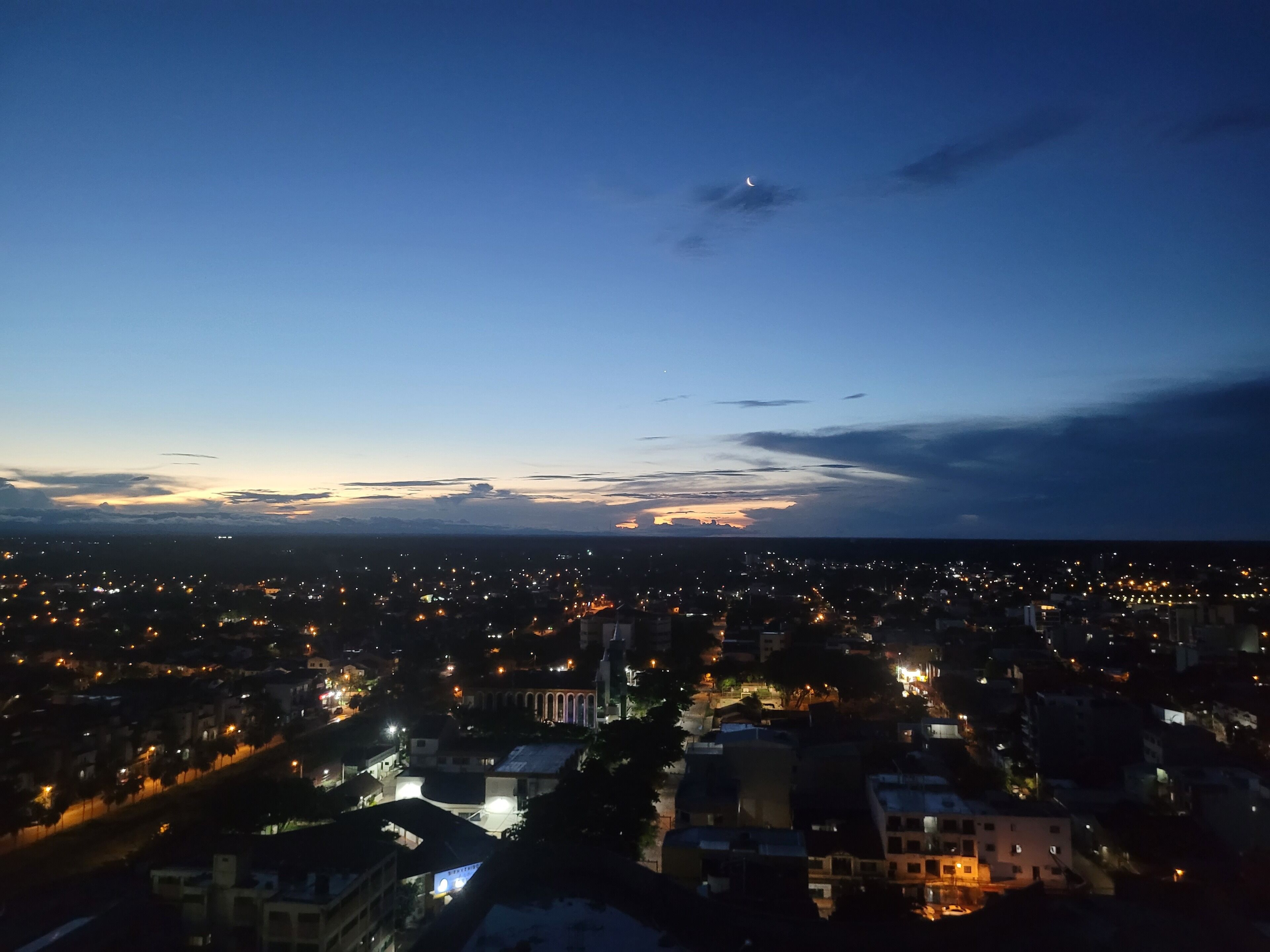 Un paisaje urbano al atardecer con una luna creciente en el cielo.