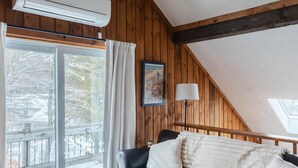A cozy room with a leather sofa, a round wooden coffee table, and a large window with a view of a snowy deck. - 1 Min to Cranmore - Sleeps 12 - 4 levels - Arcade Bunk Room- 3 Min to Downtown (North Conway)