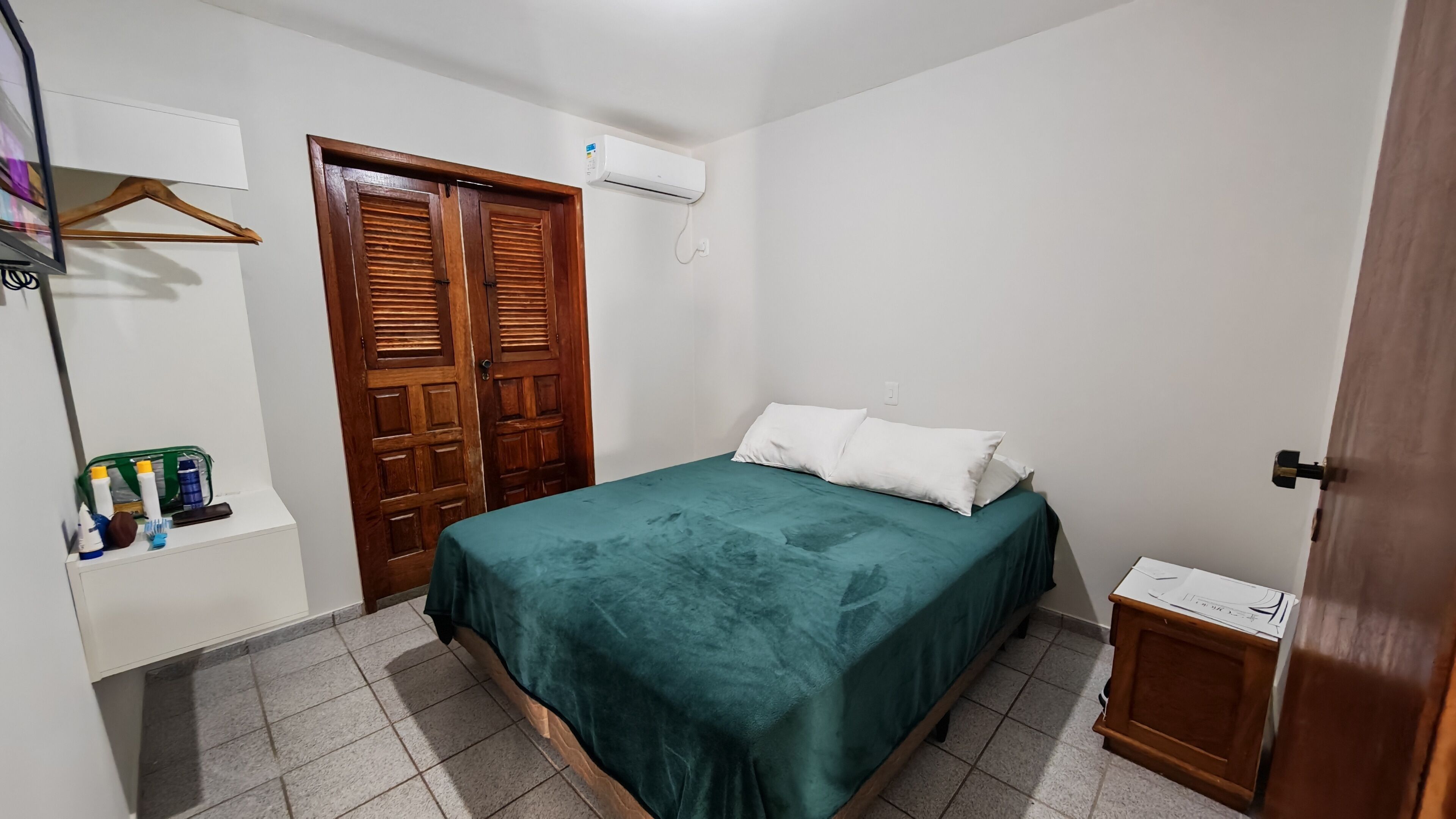 Un dormitori amb un llit, un armari, una taula de nit i aire condicionat fixat a la paret.