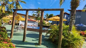 Un espace piscine agrémenté de pergolas en bois, de coins salon extérieurs et de palmiers.