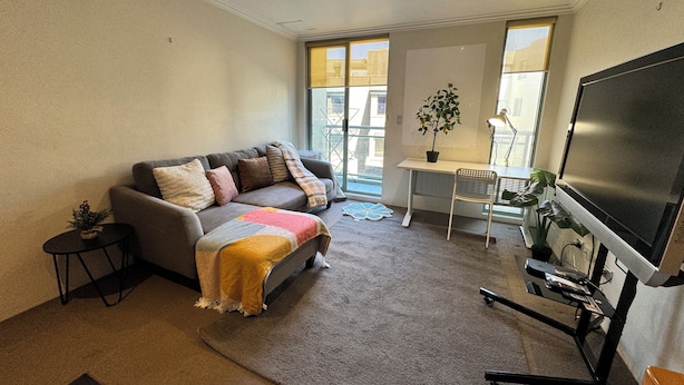 Ein Wohnzimmer mit einem grauen Sofa, einem kleinen Tisch, einem Fernseher und einer Pflanze.