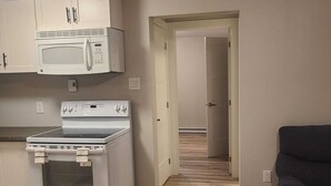 A kitchen with white cabinets, a microwave, and a stove. There is a dark-colored sofa in the living area. - Cozy Private One-Bedroom Suite With Separate Entrance—Dining set & kitchen (Dieppe)