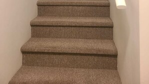 A carpeted staircase with a handrail, leading to a landing with a door and a light fixture. - Cozy Private One-Bedroom Suite With Separate Entrance—Dining set & kitchen (Dieppe)
