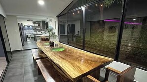 Una cocina moderna con una larga mesa de madera y bancos, una planta en maceta y vistas a un jardín a través de amplios ventanales.