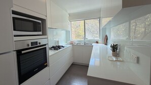 Una cucina moderna con mobili bianchi, forno integrato, microonde e piano cottura a gas. Una finestra offre luce naturale e vista all'esterno.