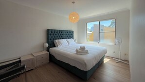 Una camera da letto moderna con un letto grande, un comodino, una panca, una lampada da terra e una finestra con vista sulla città.