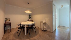 Zona pranzo con tavolo rotondo, quattro sedie, lampadario a sospensione, una piccola pianta in vaso e un tavolino con una cornice.