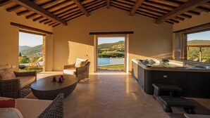 Een ruime kamer met een hoge nok, een jacuzzi en uitzicht op een meer en heuvels.