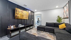 Ein modernes Wohnzimmer mit einem Ecksofa, einem flachbildfernseher an der Wand, einer Unterhaltungsecke aus dunklem Holz und einem gemusterten Teppich.