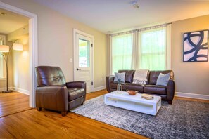 A living room with a brown leather sofa, a matching armchair, a white coffee table, and a patterned rug.