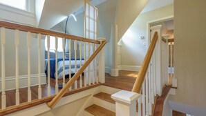 A staircase with white railings and wooden steps, leading to a bedroom with a bed and a window.