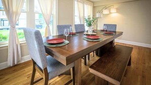 A dining area with a wooden table, grey chairs, and a bench. There are wine glasses and plates on the table.