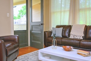 A living room with a brown leather sofa, a white coffee table, and a door leading to an outdoor area. - Historic Westcott 3-Bed Suite (Syracuse)