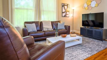 Ett vardagsrum med en brun lädersoffa, ett vitt soffbord och en platt-TV som står på ett svart TV-bord.