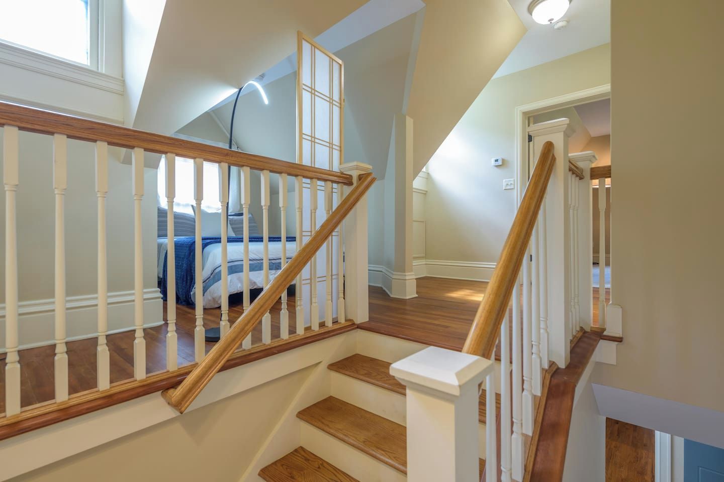 Un escalier avec des marches en bois et des balustrades blanches, menant à une chambre à coucher avec un lit et une fenêtre.