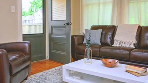 A living room with a brown leather sofa, a white coffee table, and a door leading to a balcony.