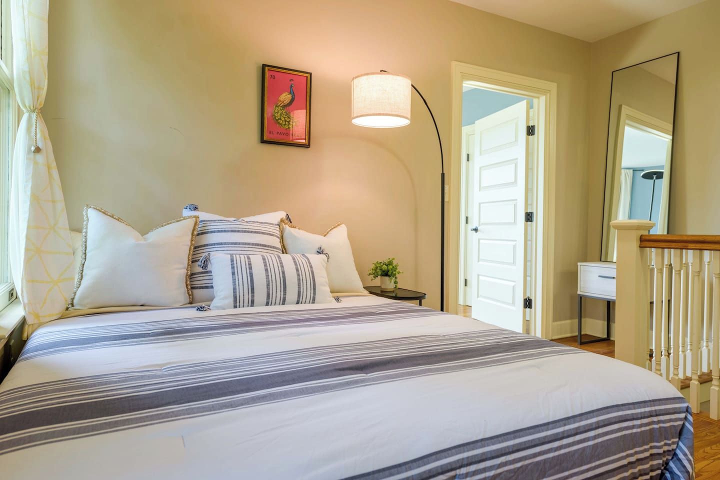 A bedroom with a bed, pillows, a bedside table with a lamp, a mirror, and a door.