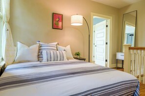 Une chambre à coucher avec un lit, des oreillers, une table de chevet avec une lampe, un miroir et une porte.