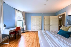 Ein Schlafzimmer mit einem Bett, einem Schreibtisch und einem Stuhl. Es gibt zwei Türen und ein Fenster.