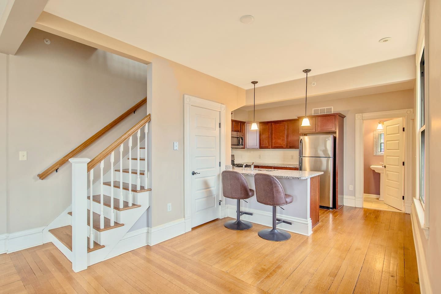 A modern kitchen with a central island, stainless steel appliances, and a wooden staircase.
