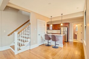 Une cuisine moderne dotée d’un îlot central, d’appareils électroménagers en acier inoxydable et d’un escalier en bois.